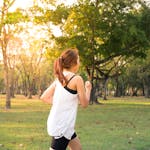 A woman jogging through a forest park in the early morning sunshine, enjoying a healthy lifestyle.
