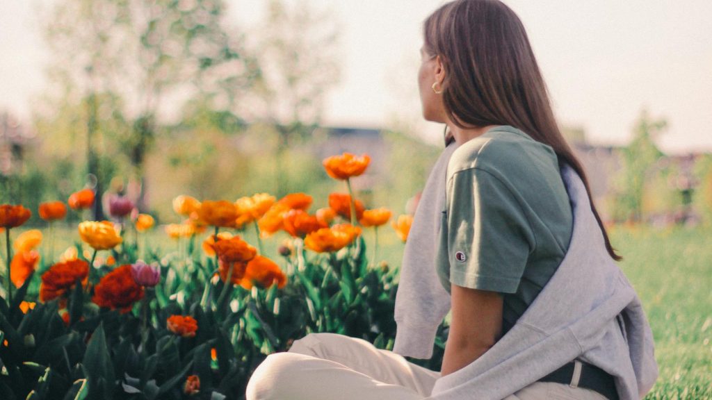 A woman enjoys a peaceful moment sitting among vibrant flowers in a park.