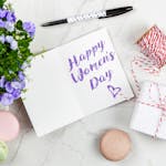Celebrate Women's Day with a thoughtful greeting card, flowers, macarons, and a wrapped gift on a white background.